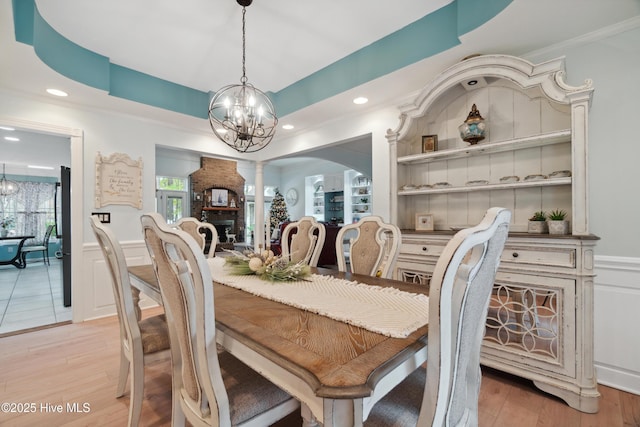 dining area with a notable chandelier, light wood-style flooring, built in shelves, and ornate columns