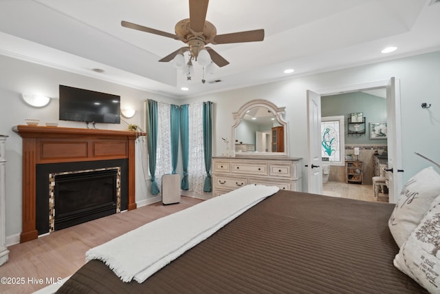 bedroom with crown molding, light wood-type flooring, a tray ceiling, recessed lighting, and a glass covered fireplace