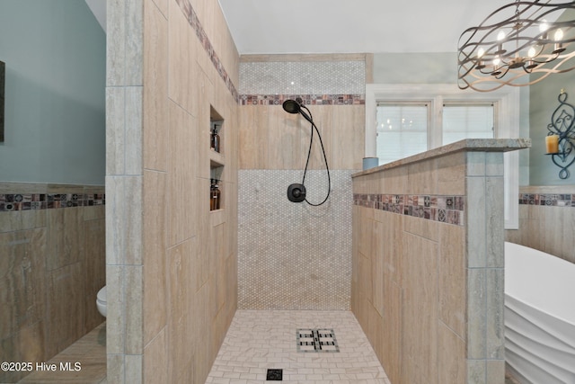 full bathroom featuring a walk in shower, a chandelier, a wainscoted wall, toilet, and tile walls