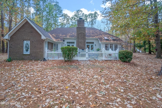 back of house with a fenced front yard, brick siding, roof with shingles, and a chimney