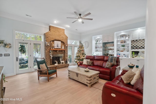 living area featuring light wood-type flooring, a brick fireplace, ceiling fan, and ornamental molding