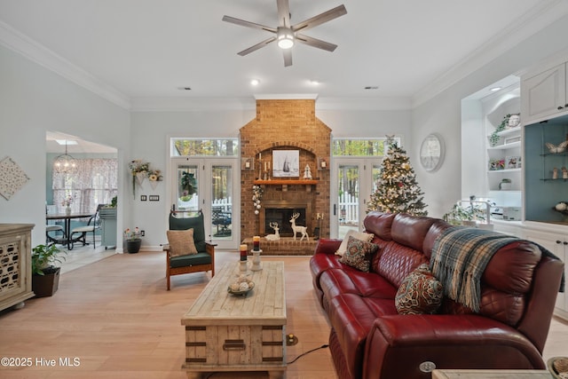 living room with a fireplace, ceiling fan with notable chandelier, light wood-style floors, and ornamental molding