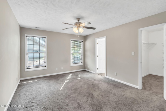 carpeted spare room with a textured ceiling, a ceiling fan, visible vents, and baseboards