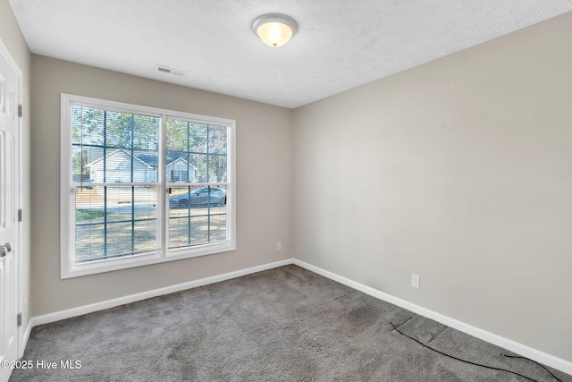 carpeted empty room featuring a wealth of natural light, visible vents, a textured ceiling, and baseboards