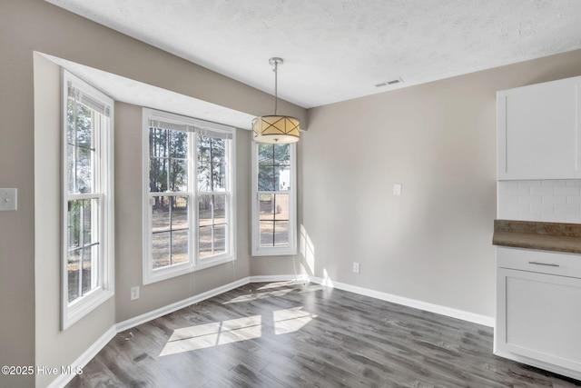 unfurnished dining area featuring dark wood finished floors, a healthy amount of sunlight, visible vents, and baseboards