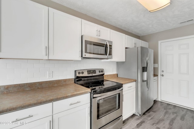 kitchen featuring visible vents, light wood-type flooring, decorative backsplash, appliances with stainless steel finishes, and white cabinetry