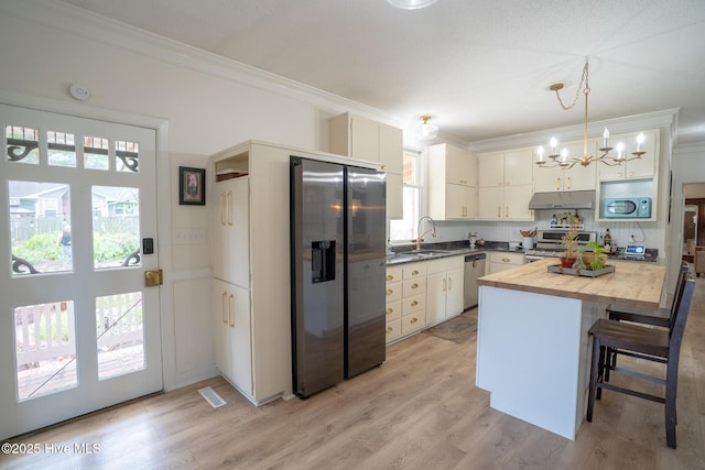 661 Main St, Swansboro, NC 28584 - kitchen with appliances with stainless steel finishes, under cabinet range hood, butcher block counters, ornamental molding, and a chandelier