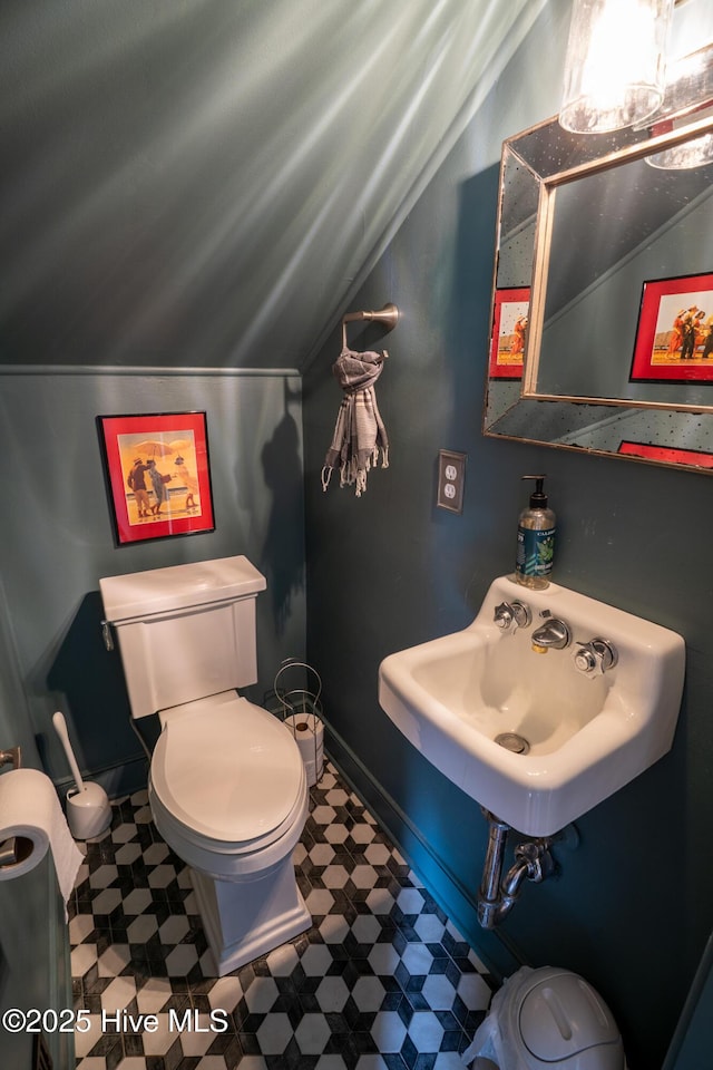 half bathroom featuring lofted ceiling, toilet, baseboards, tile patterned floors, and a sink