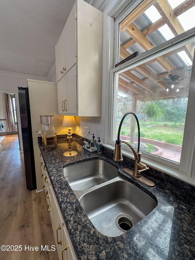 kitchen with a textured ceiling, hardwood / wood-style flooring, a sink, white cabinets, and dark stone countertops