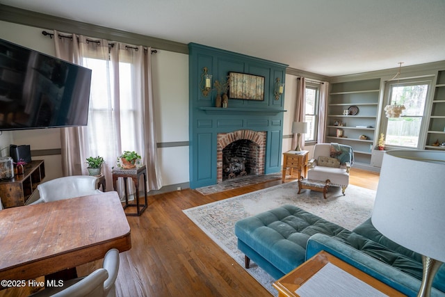 living room with a brick fireplace, baseboards, ornamental molding, and wood finished floors
