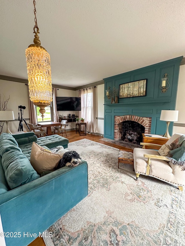 living area with crown molding, an inviting chandelier, wood finished floors, a fireplace, and a textured ceiling