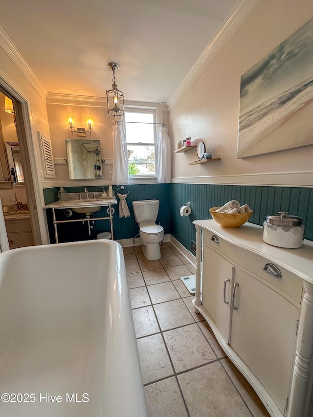 bathroom featuring crown molding, a wainscoted wall, toilet, and a freestanding tub