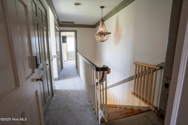 hall with a notable chandelier, carpet floors, an upstairs landing, visible vents, and ornamental molding