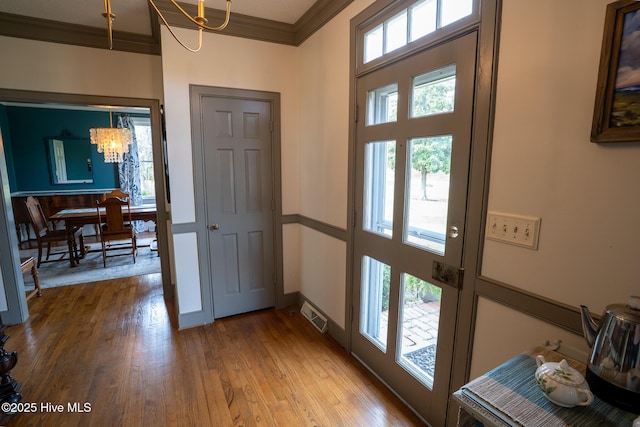foyer entrance with an inviting chandelier, ornamental molding, wood finished floors, and visible vents