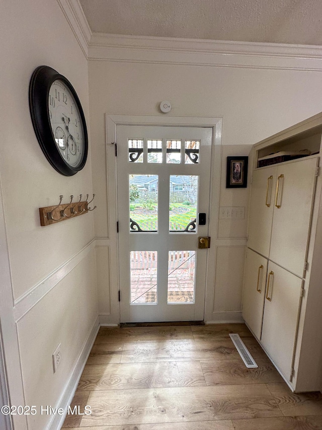 doorway to outside featuring visible vents, light wood-style flooring, and crown molding