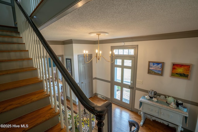 interior space with a textured ceiling, stairs, wood finished floors, visible vents, and ornamental molding