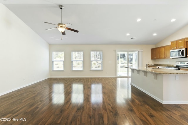 kitchen with a wealth of natural light, brown cabinets, appliances with stainless steel finishes, and lofted ceiling