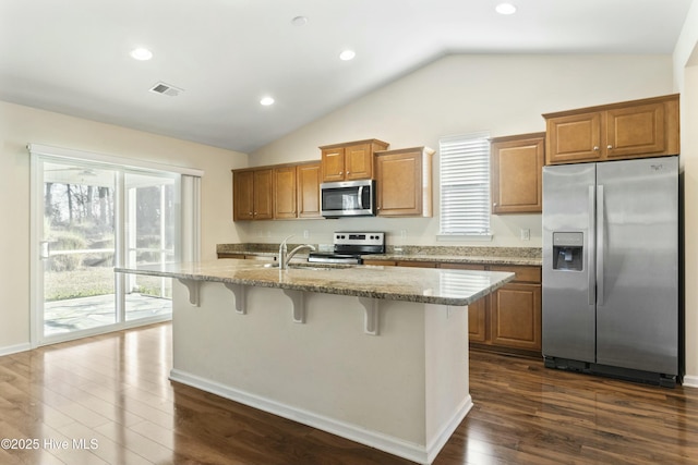 kitchen featuring brown cabinetry, visible vents, a center island with sink, a sink, and appliances with stainless steel finishes