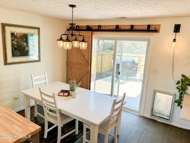 dining area featuring visible vents, a textured ceiling, a barn door, dark colored carpet, and baseboards