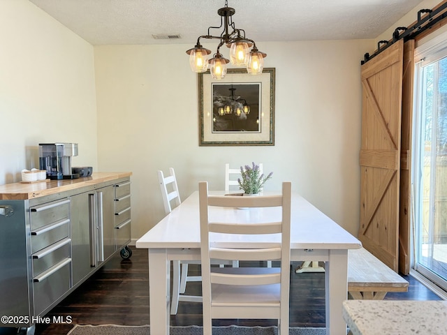 dining space with a barn door, dark wood-style floors, visible vents, and a textured ceiling