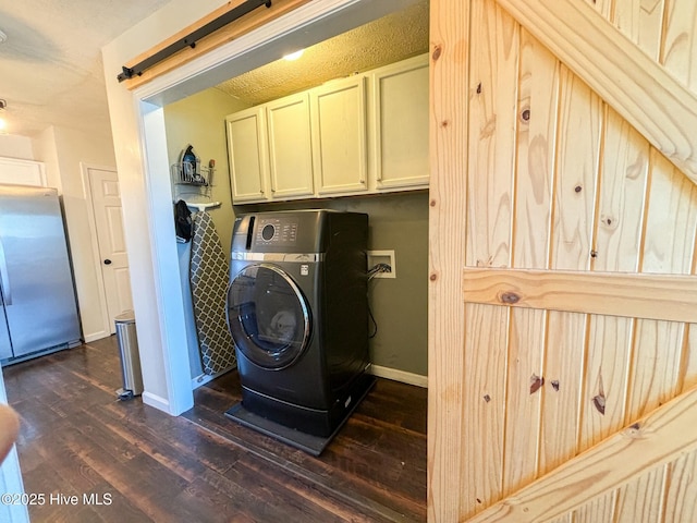 clothes washing area with dark wood finished floors, a barn door, cabinet space, baseboards, and washer / dryer