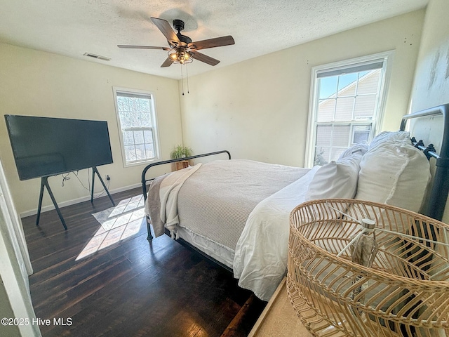 bedroom featuring a ceiling fan, wood finished floors, visible vents, baseboards, and a textured ceiling