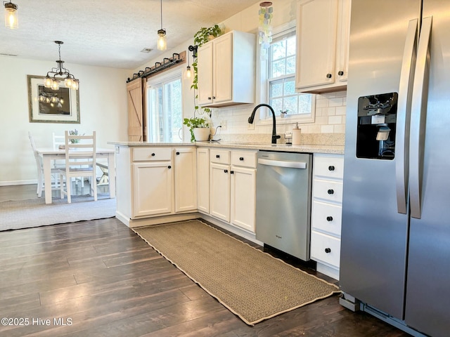 kitchen featuring a peninsula, dark wood-style flooring, appliances with stainless steel finishes, tasteful backsplash, and a chandelier