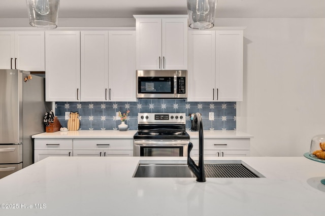 kitchen with a sink, tasteful backsplash, white cabinetry, appliances with stainless steel finishes, and light countertops