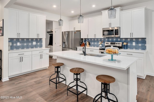 kitchen with light wood-style flooring, a sink, white cabinets, appliances with stainless steel finishes, and a kitchen bar