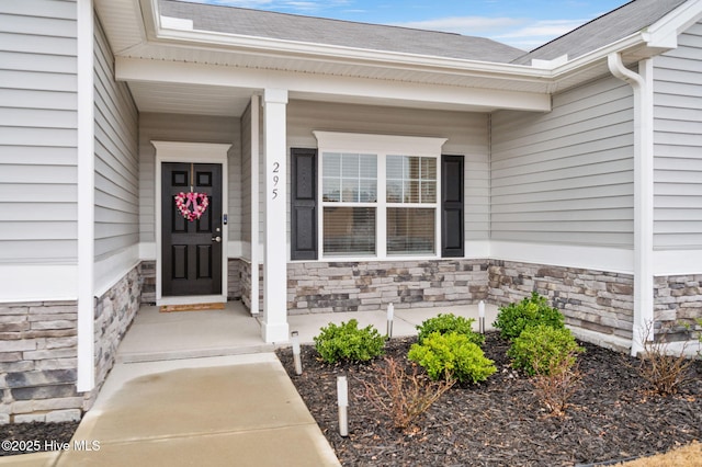 entrance to property featuring stone siding and a shingled roof