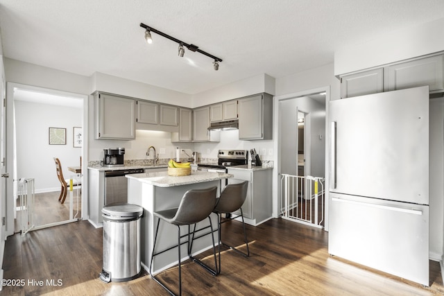 kitchen with gray cabinetry, a kitchen breakfast bar, dark wood finished floors, a center island, and stainless steel appliances