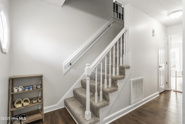 stairway with visible vents, a textured ceiling, baseboards, and wood finished floors