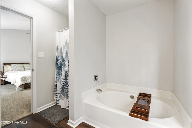 ensuite bathroom with baseboards, a garden tub, a shower with curtain, a textured ceiling, and ensuite bath