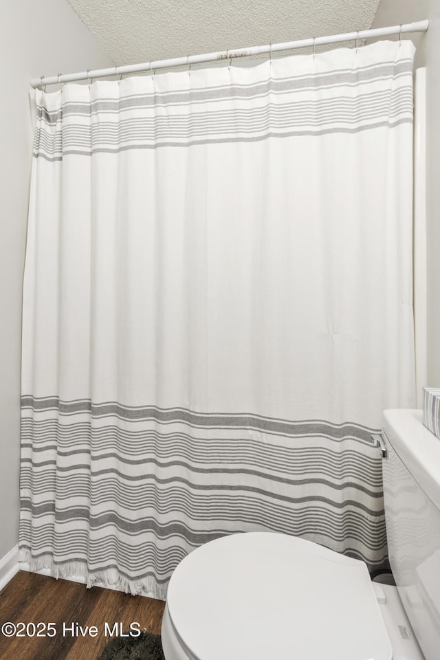 full bath with curtained shower, toilet, wood finished floors, and a textured ceiling