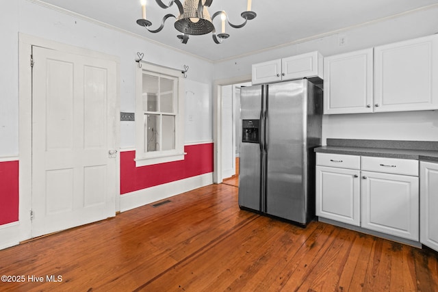 kitchen with dark countertops, stainless steel fridge with ice dispenser, ornamental molding, an inviting chandelier, and white cabinetry