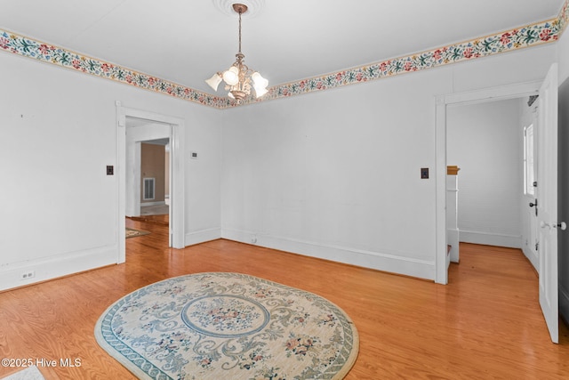 empty room with visible vents, a notable chandelier, wood finished floors, and baseboards