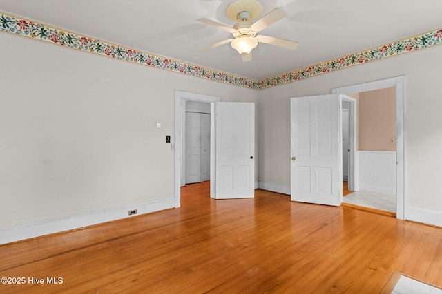 empty room featuring wainscoting, light wood-style flooring, baseboards, and a ceiling fan