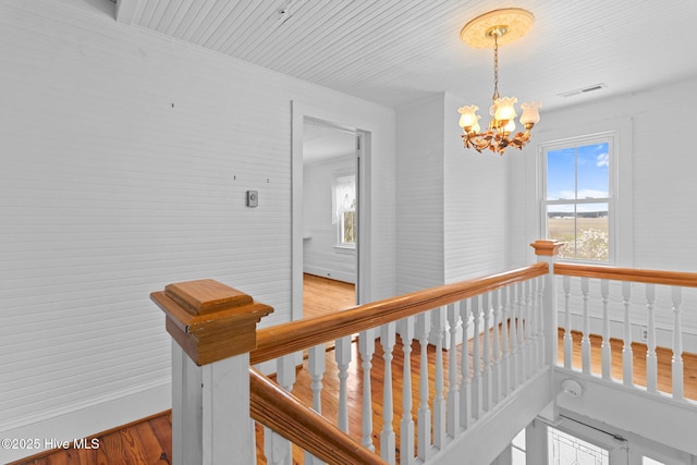 hall featuring an upstairs landing, visible vents, a chandelier, and wood finished floors