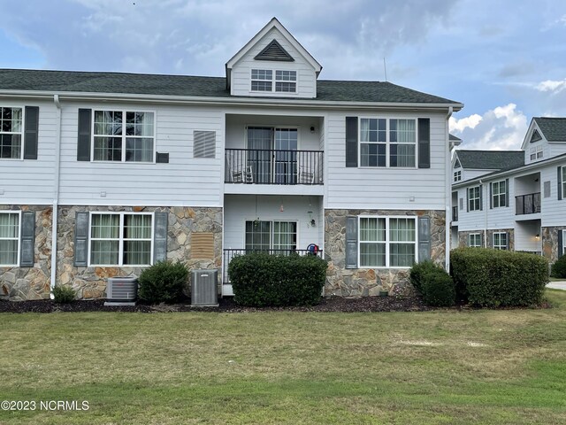 view of front of property featuring a front lawn, stone siding, and central AC