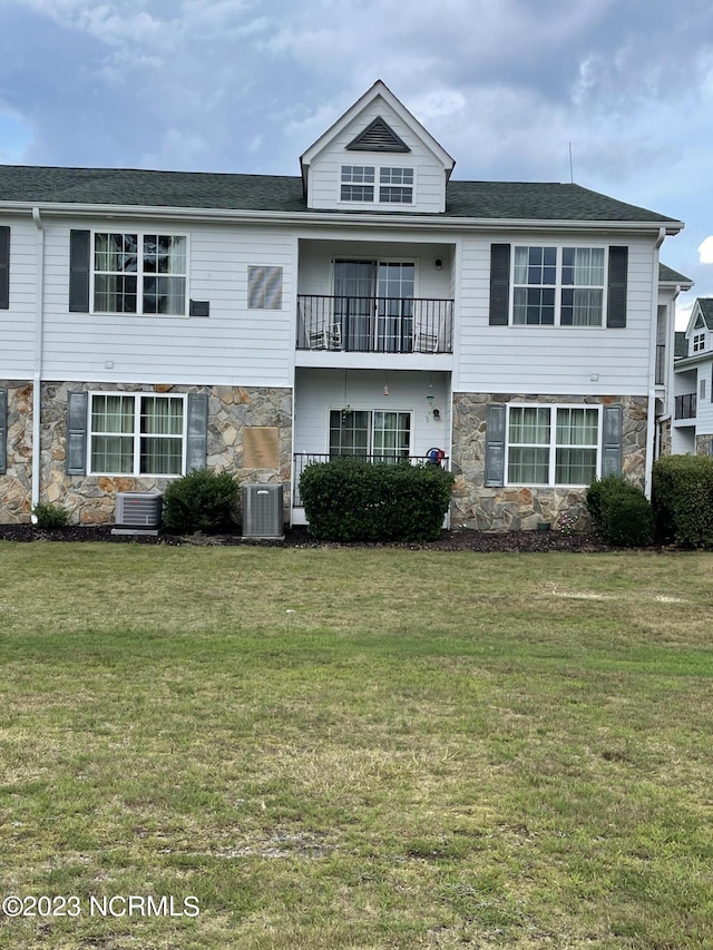 view of front facade with a front lawn, a balcony, central AC unit, and stone siding