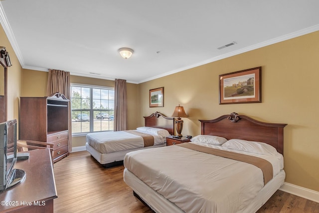 bedroom featuring crown molding, wood finished floors, baseboards, and visible vents