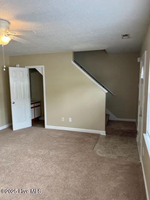 unfurnished living room featuring visible vents, a textured ceiling, carpet, ceiling fan, and stairs