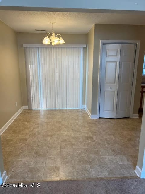 empty room with a notable chandelier, baseboards, and a textured ceiling