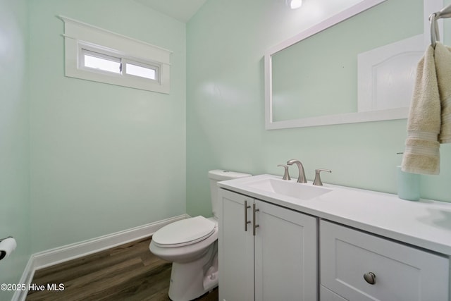 half bathroom featuring toilet, vanity, baseboards, and wood finished floors