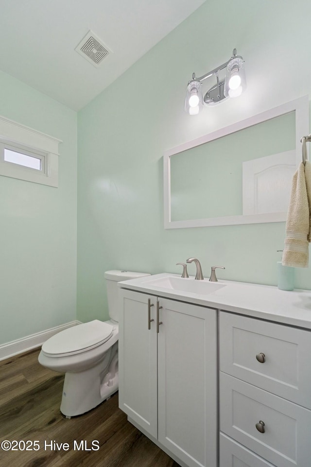 half bathroom featuring visible vents, toilet, vanity, and wood finished floors