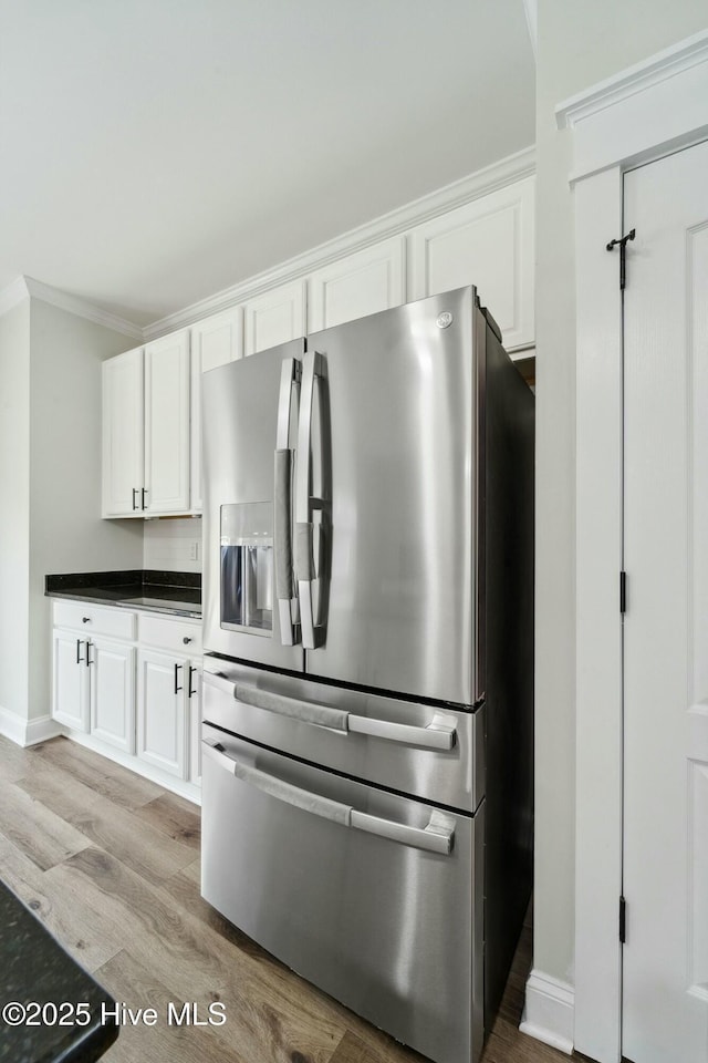 kitchen with dark countertops, crown molding, stainless steel fridge with ice dispenser, light wood-type flooring, and white cabinets