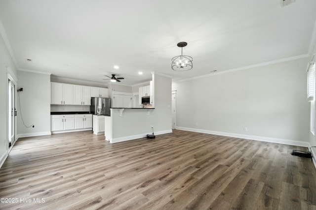 unfurnished living room with ceiling fan with notable chandelier, recessed lighting, light wood-style floors, crown molding, and baseboards