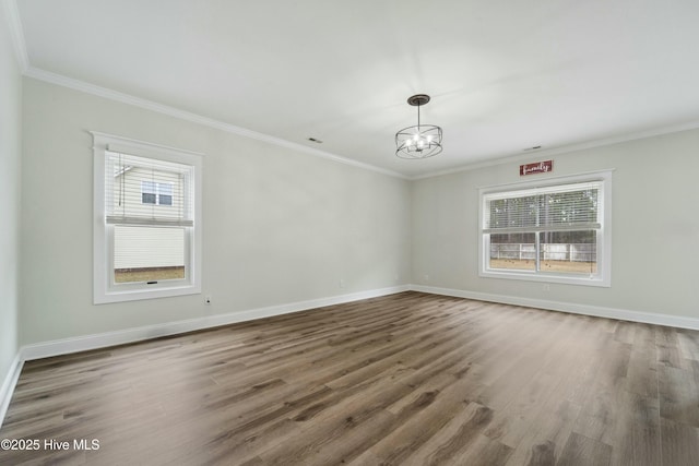 empty room with plenty of natural light, crown molding, an inviting chandelier, and wood finished floors