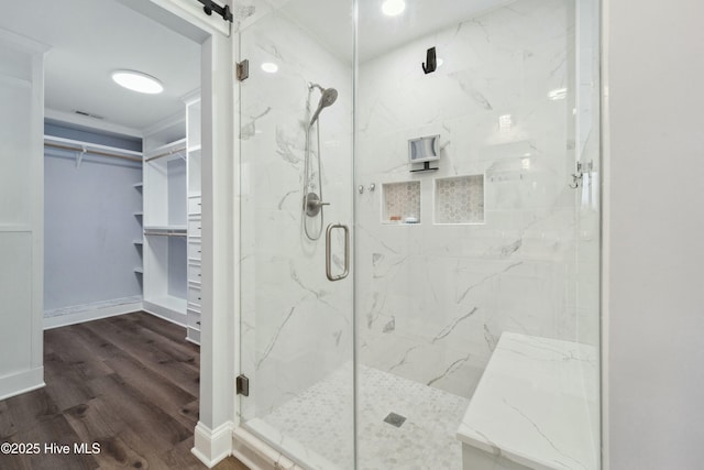 full bath featuring a marble finish shower, a walk in closet, baseboards, and wood finished floors