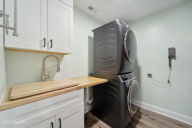 laundry area with wood finished floors, visible vents, baseboards, cabinet space, and stacked washer and clothes dryer